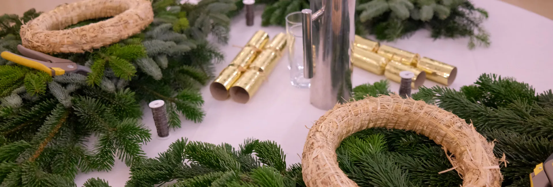 Materials for making Christmas wreaths, including fir branches, straw rings, pruning shears and gold decorations