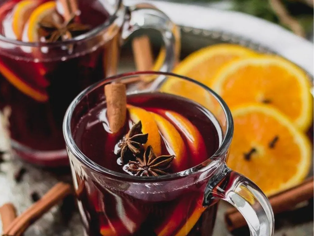 Two glass mugs of mulled wine garnished with orange slices, cinnamon sticks and star anise.