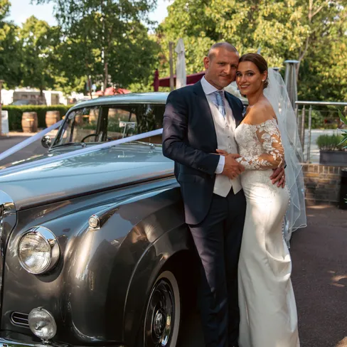 Bride and groom posing beside a grey vintage wedding car outdoors