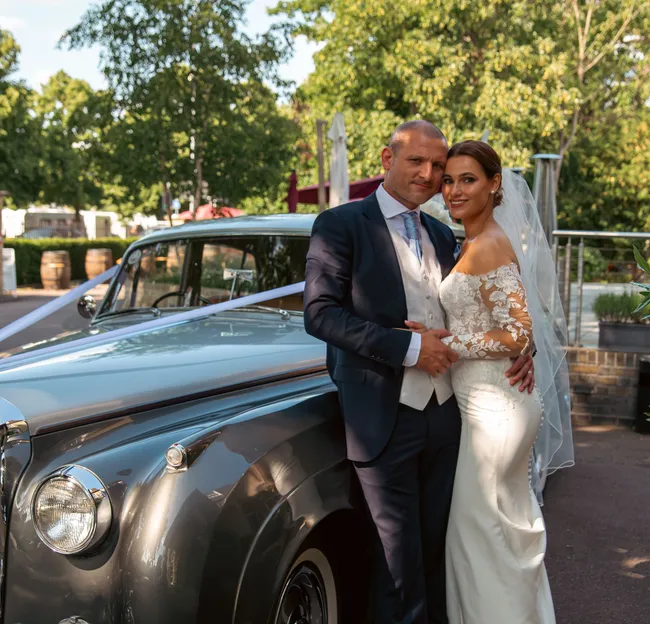Bride and groom posing beside a grey vintage wedding car outdoors