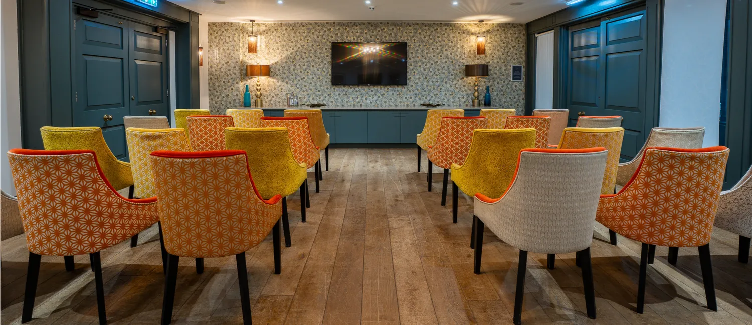 Rows of colourful upholstered chairs facing a wall-mounted television in an elegant meeting room