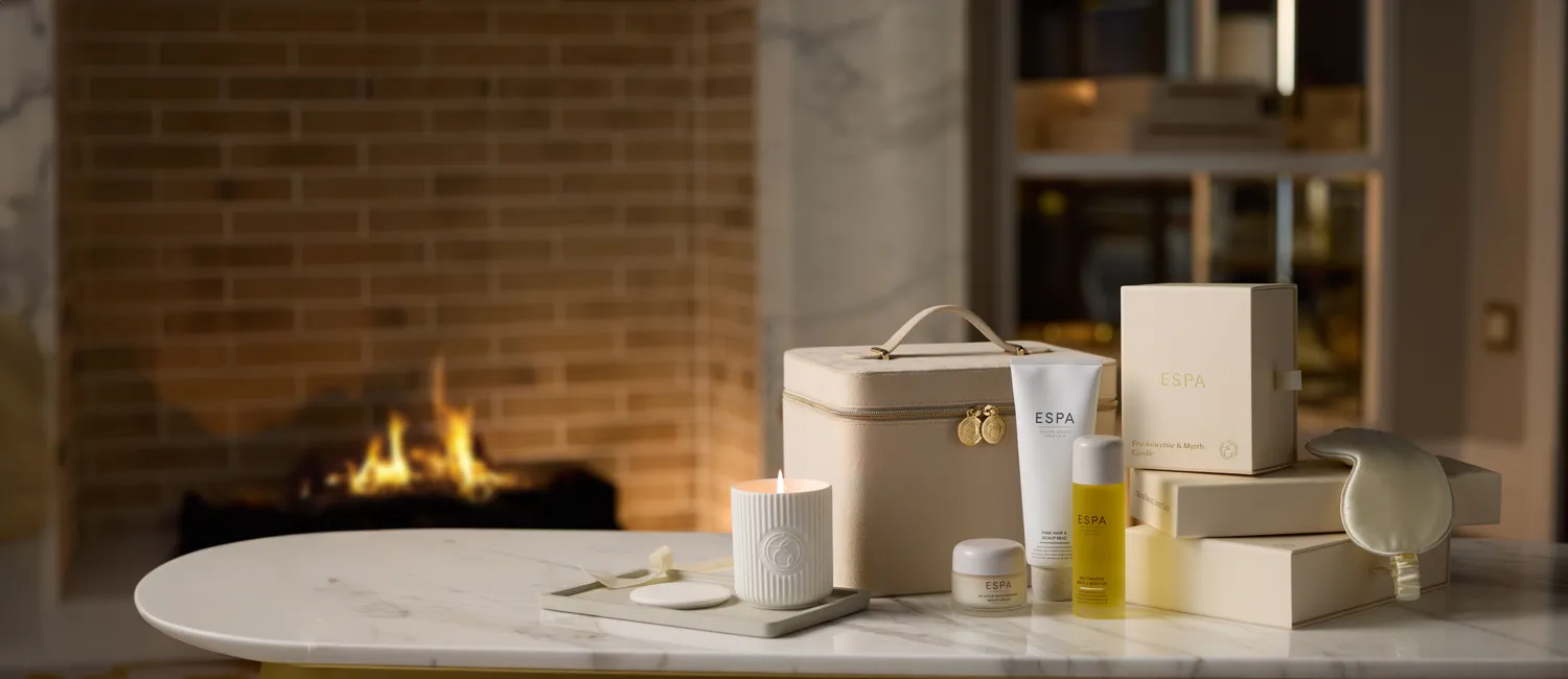 ESPA skincare gifts, a lit candle and a cream toiletry case on a marble table beside a fireplace