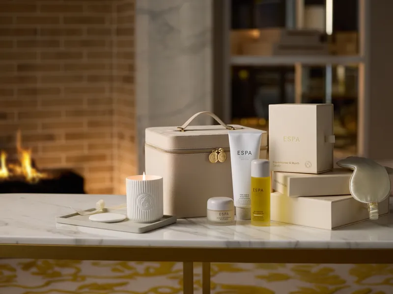 ESPA skincare gifts, a lit candle and a cream toiletry case on a marble table beside a fireplace