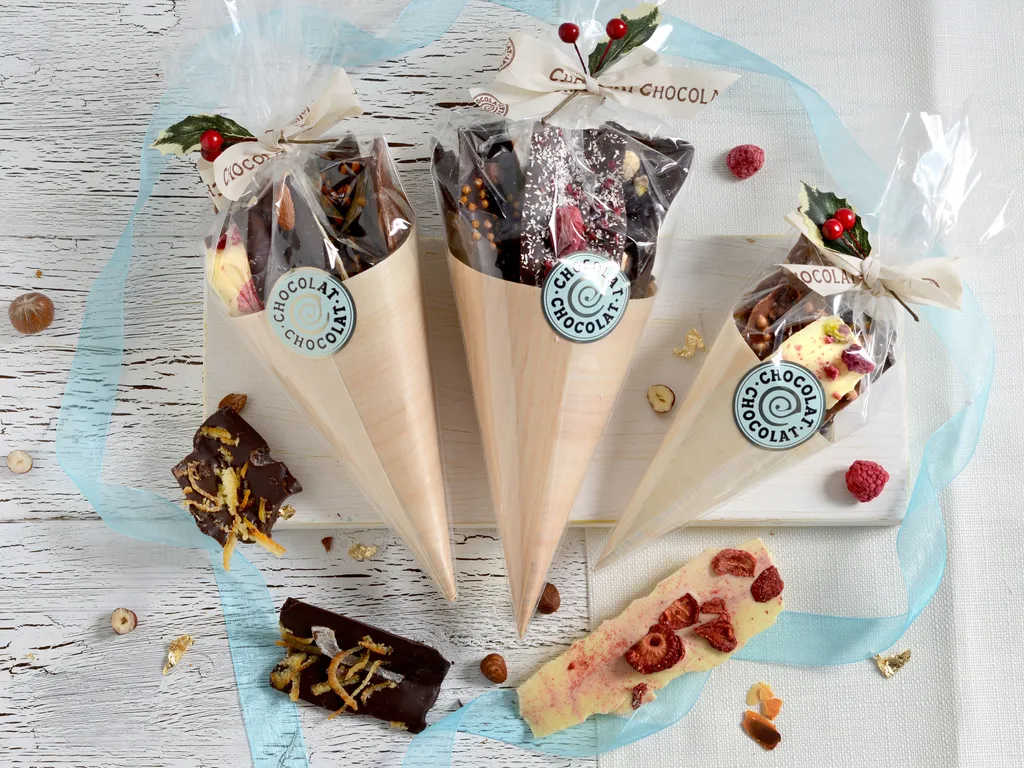 Three Christmas chocolate bouquets in clear wrapping, decorated with holly and surrounded by chocolate pieces and pale blue ribbon.