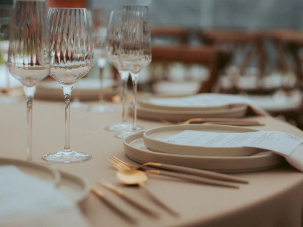 Elegant wedding reception table set with ribbed wine glasses, cream plates, gold cutlery and printed menus.