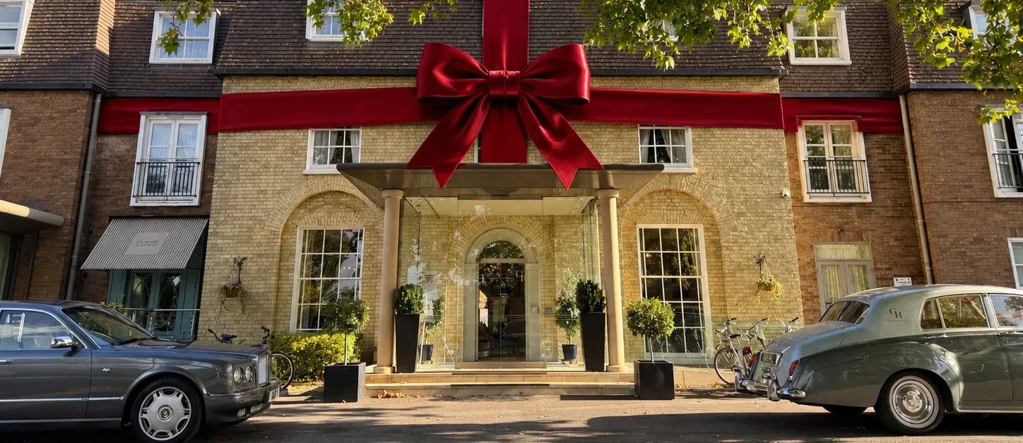 Hotel façade wrapped in a giant red ribbon and bow, with vintage cars parked outside