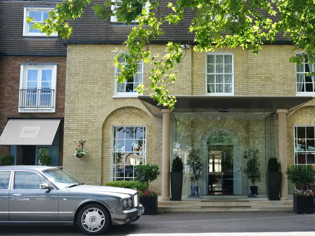 Hotel entrance with glass doors, potted plants, parked classic car, and row of bicycles