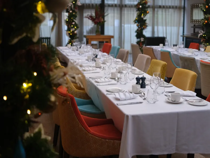 Long dining table set for a festive meal with colorful chairs and Christmas decorations.