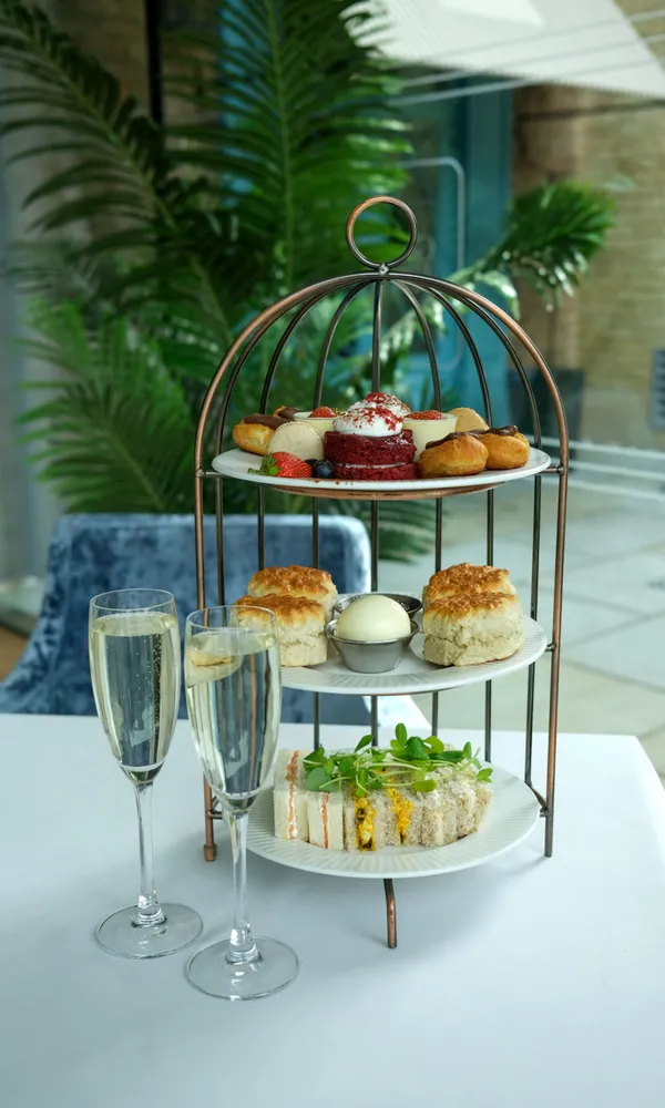 Three-tiered stand with pastries, scones, and sandwiches on a table, accompanied by two glasses of champagne.