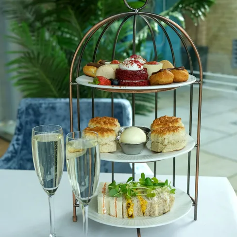 Three-tiered stand with pastries, scones, and sandwiches on a table, accompanied by two glasses of champagne.
