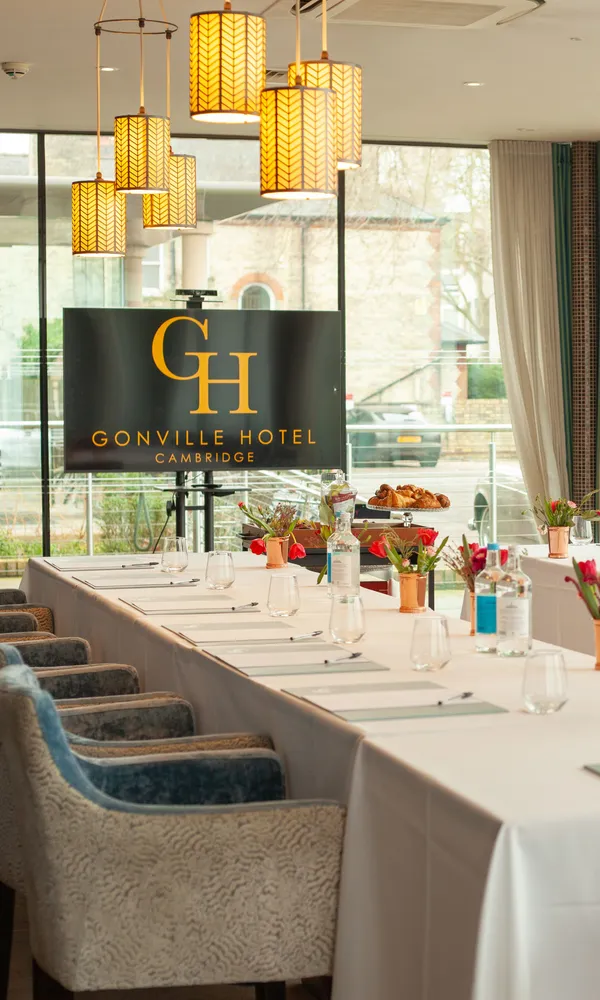 Elegant meeting room at Gonville Hotel Cambridge with U-shaped table setup, floral centerpieces, and large windows.
