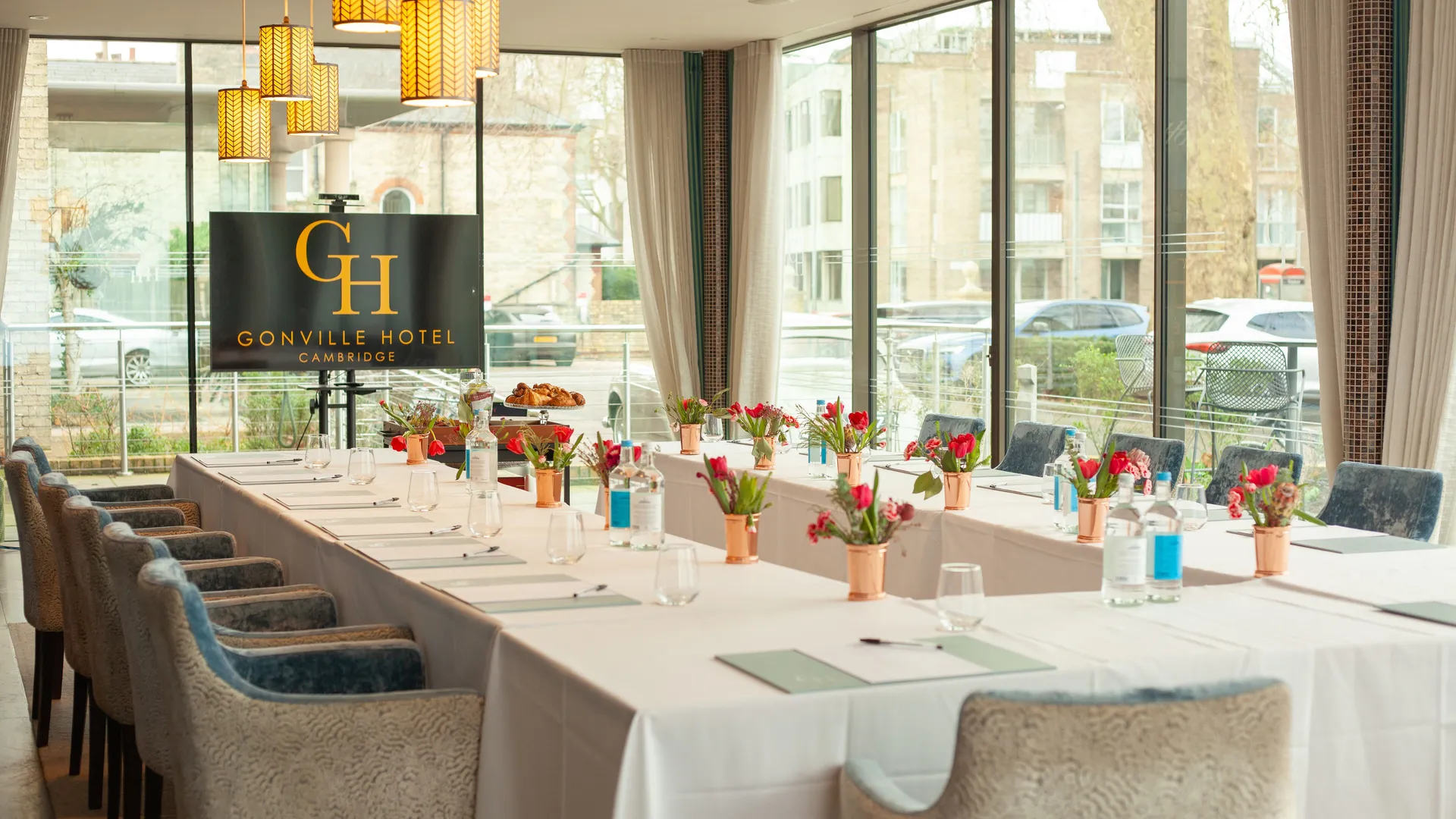 Elegant meeting room at Gonville Hotel Cambridge with U-shaped table setup, floral centerpieces, and large windows.