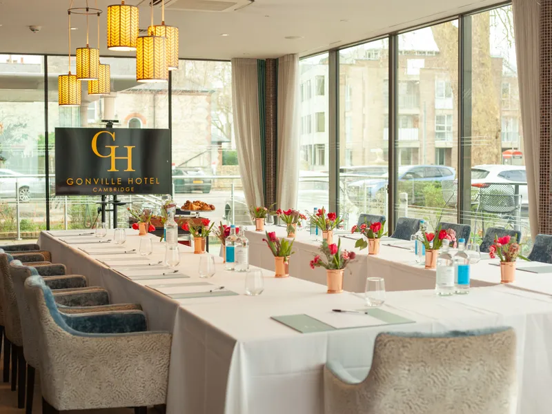 Elegant meeting room at Gonville Hotel Cambridge with U-shaped table setup, floral centerpieces, and large windows.