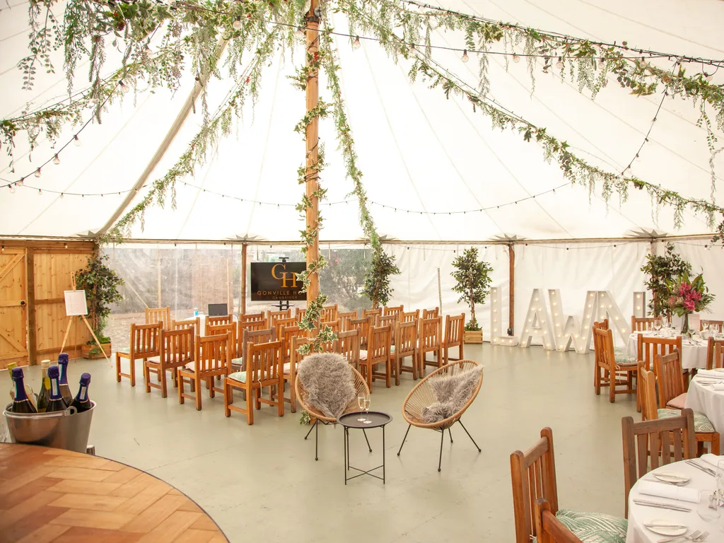Decorated teepee event tent interior with wooden chairs, round dining tables, string lights, and greenery.