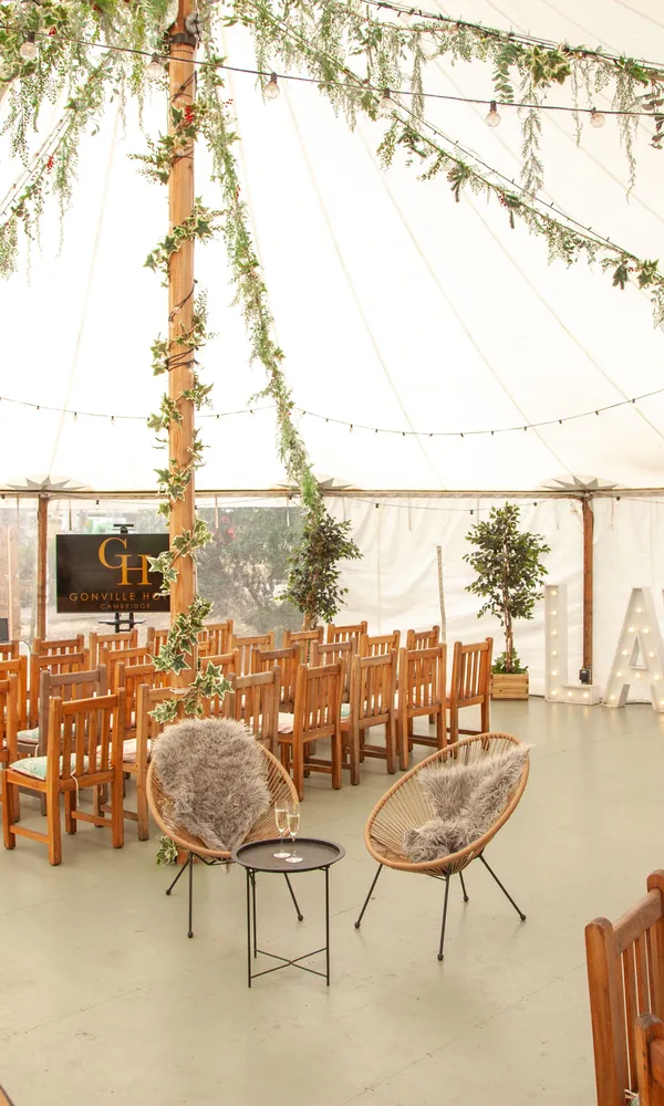 Decorated teepee event tent interior with wooden chairs, round dining tables, string lights, and greenery.