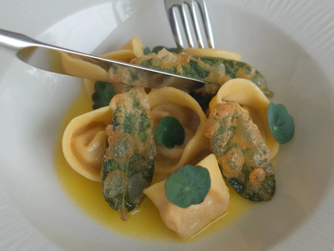 Gourmet pasta dish with stuffed pasta, crispy sage leaves, and green herbs in a yellow sauce