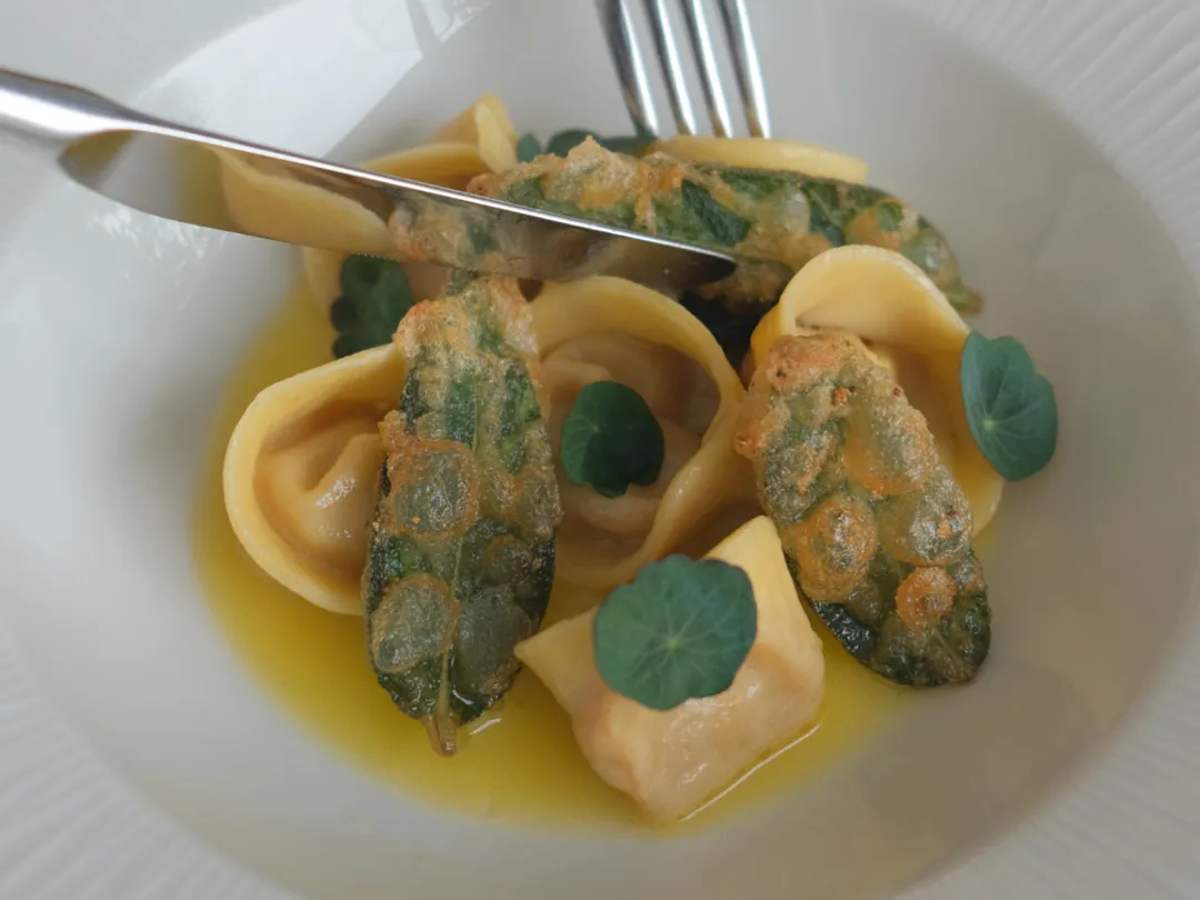 Gourmet pasta dish with stuffed pasta, crispy sage leaves, and green herbs in a yellow sauce