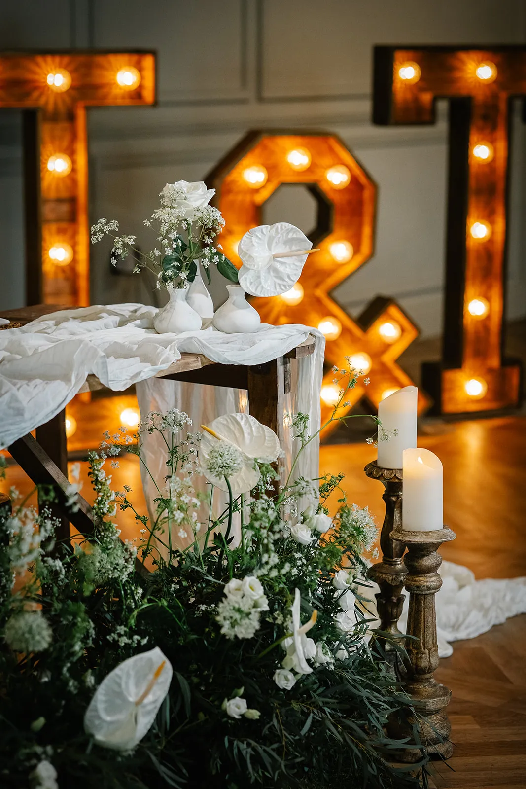 Romantic wedding display with white floral arrangements, candles and illuminated ampersand letters in an elegant indoor venue