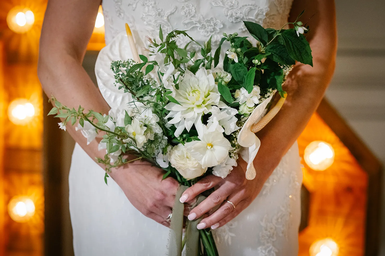Bride in a lace wedding dress holding a white and green floral bouquet on a warmly lit staircase