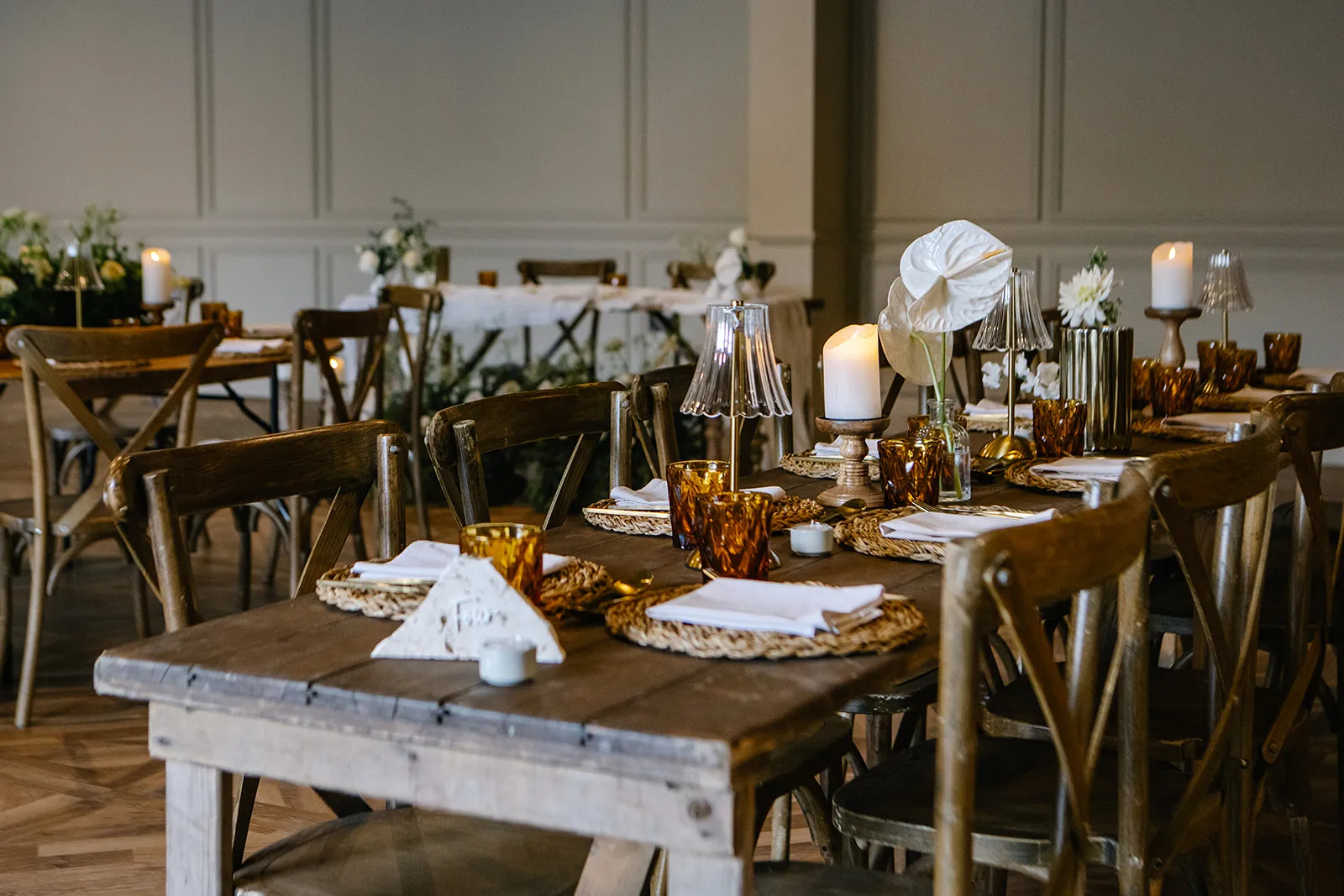 Rustic dining tables set with candles, flowers and amber glassware in an elegant event space
