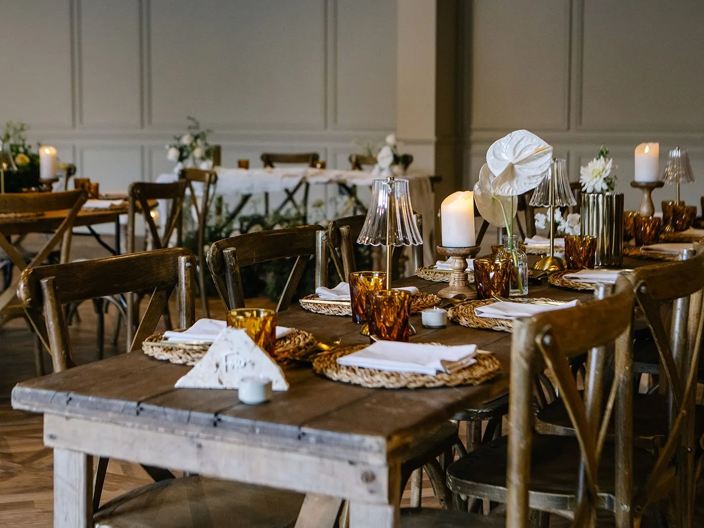 Rustic dining tables set with candles, flowers and amber glassware in an elegant event space