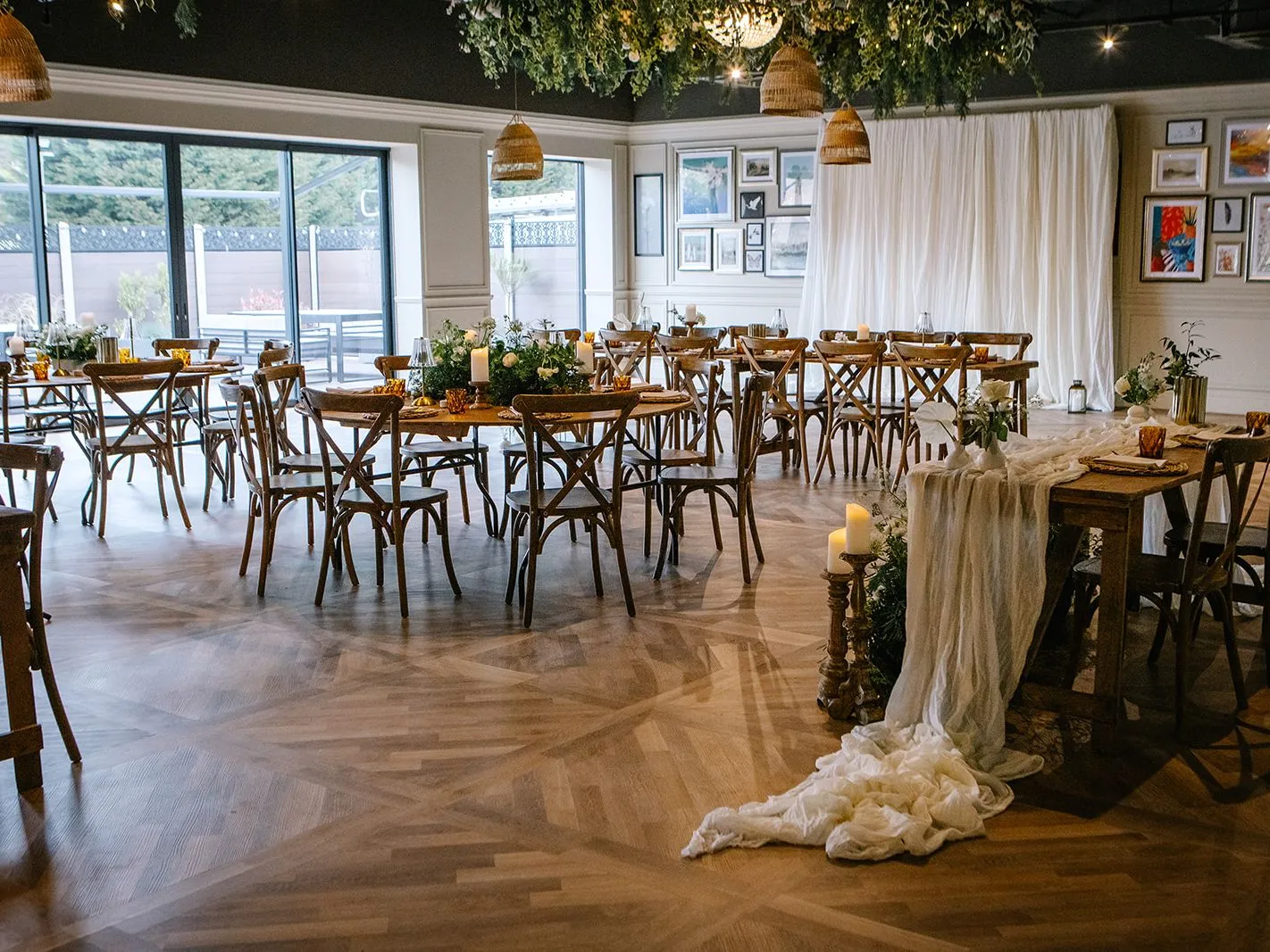 Stylish event space with wooden tables and chairs, draped fabric, candles and greenery hanging from the ceiling