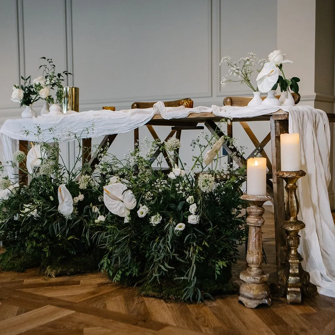Elegant wedding sweetheart table with white draped linen, candles and lush white floral arrangements in a refined indoor venue