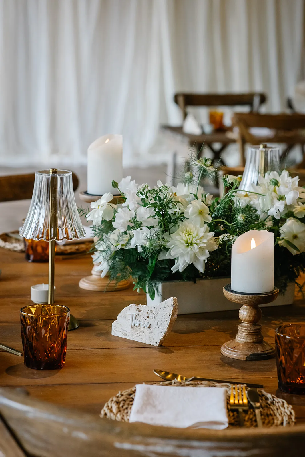 Elegant table setting with white floral centrepieces, pillar candles and amber glassware on a wooden table