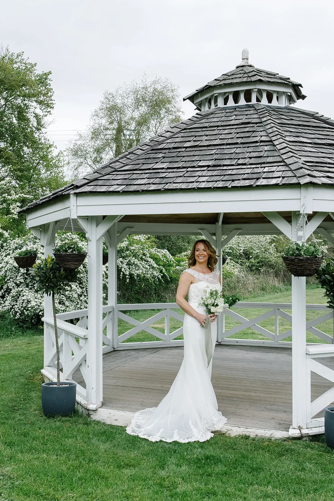 Bride standing in a white garden gazebo holding a bouquet on a lawn