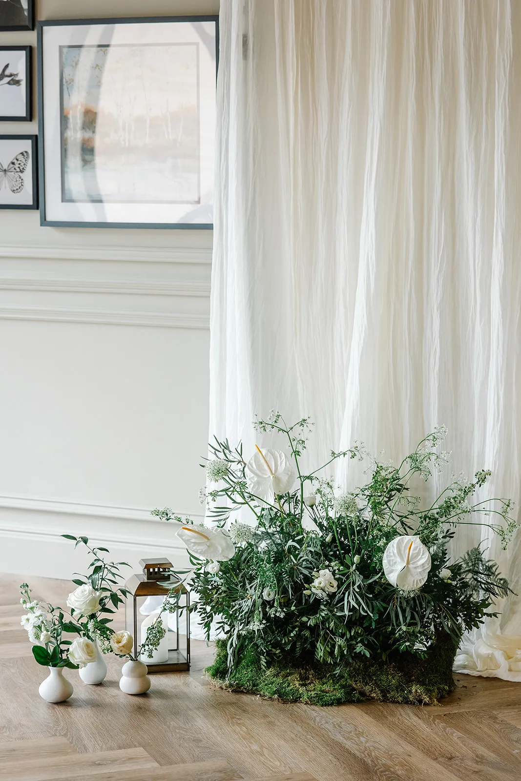 Elegant white floral arrangement with greenery, lanterns and draped fabric in a refined indoor venue