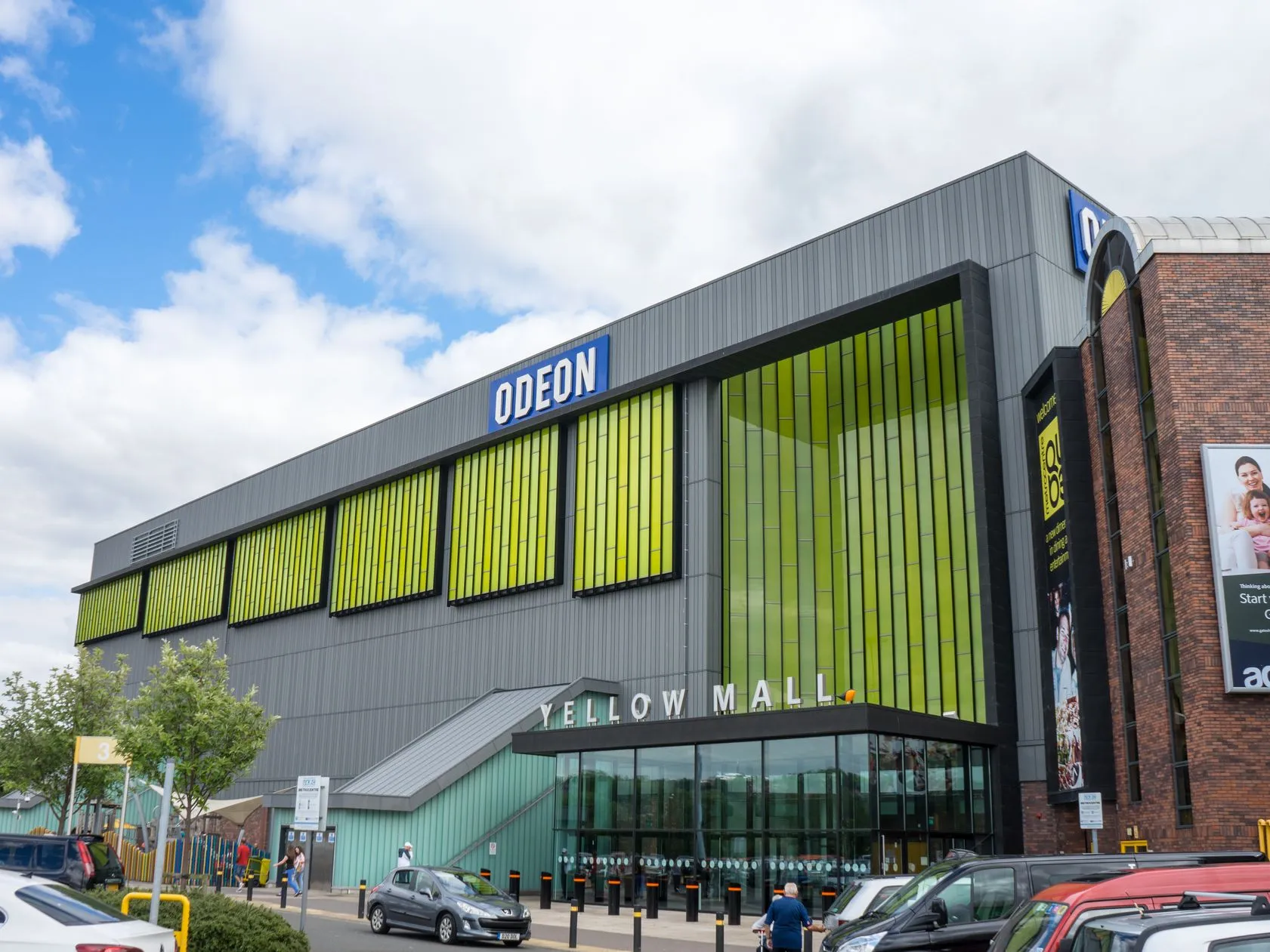 Exterior of an ODEON cinema at Yellow Mall with parked cars in the foreground under a cloudy sky