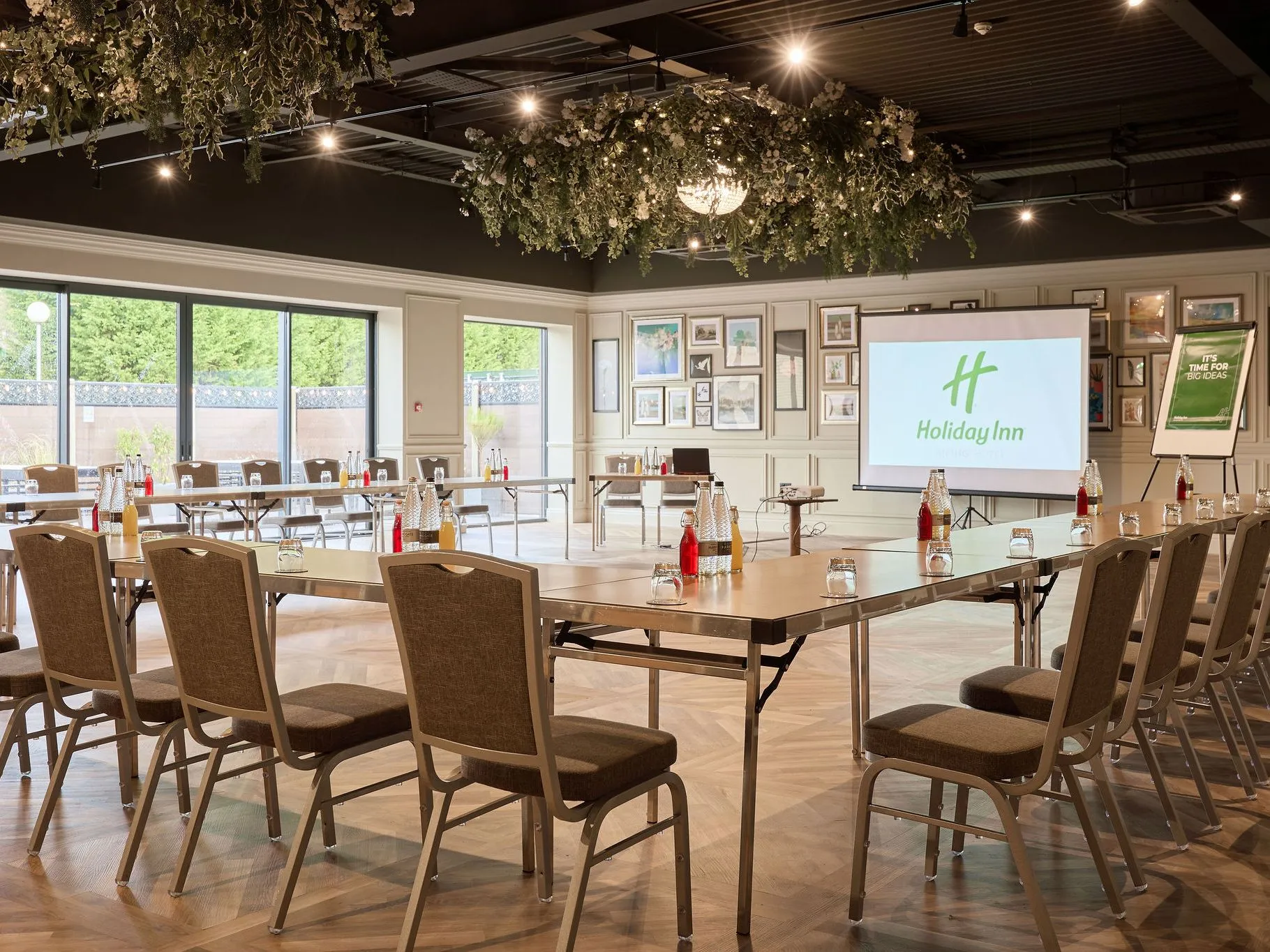 Modern Holiday Inn meeting room set up in a U-shape with chairs, projector screen and drinks on tables