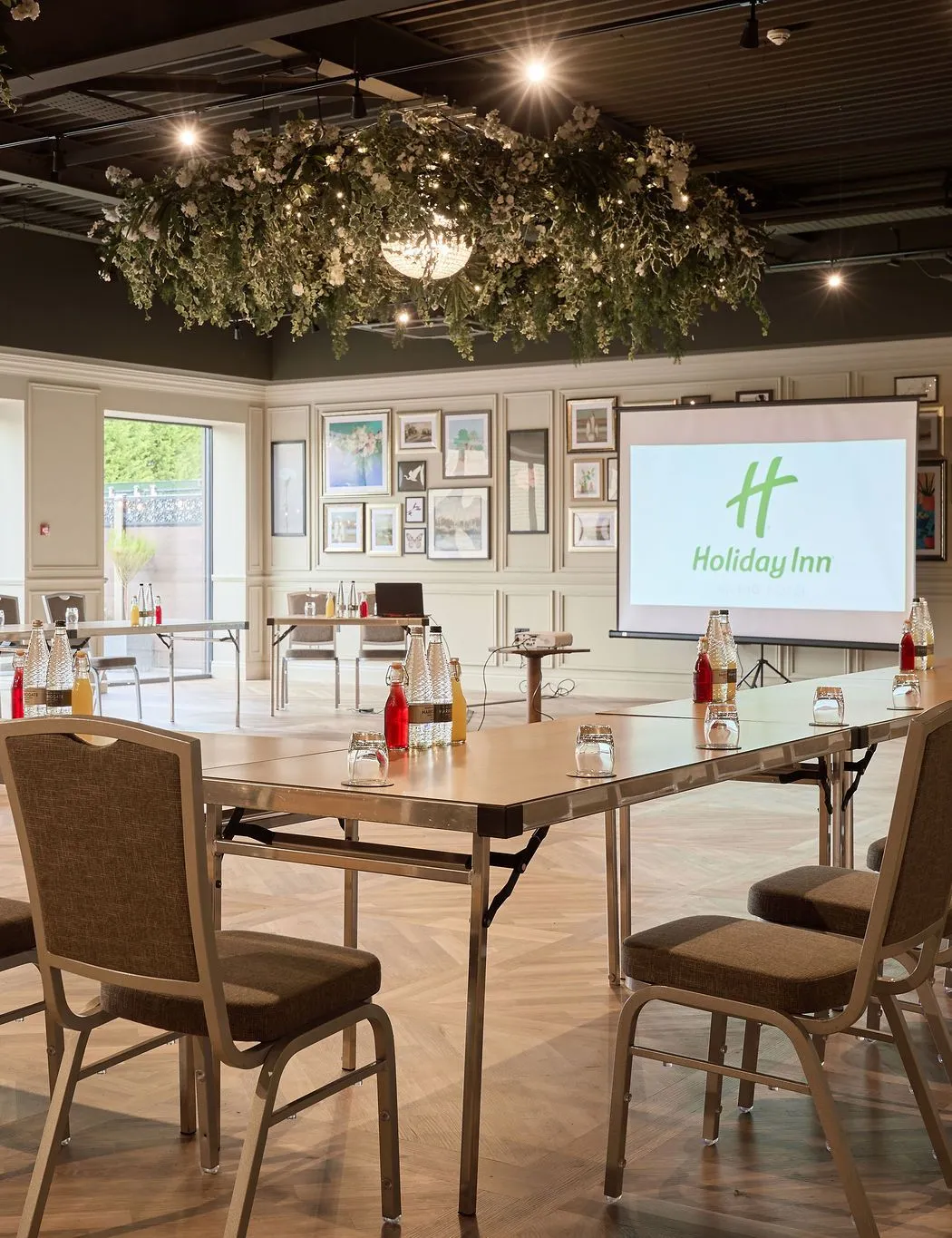 Modern Holiday Inn meeting room set up in a U-shape with chairs, projector screen and drinks on tables
