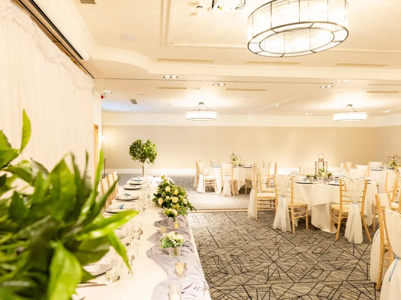 Elegantly decorated hotel function room set up for a wedding reception with round tables, floral centrepieces and draped backdrop