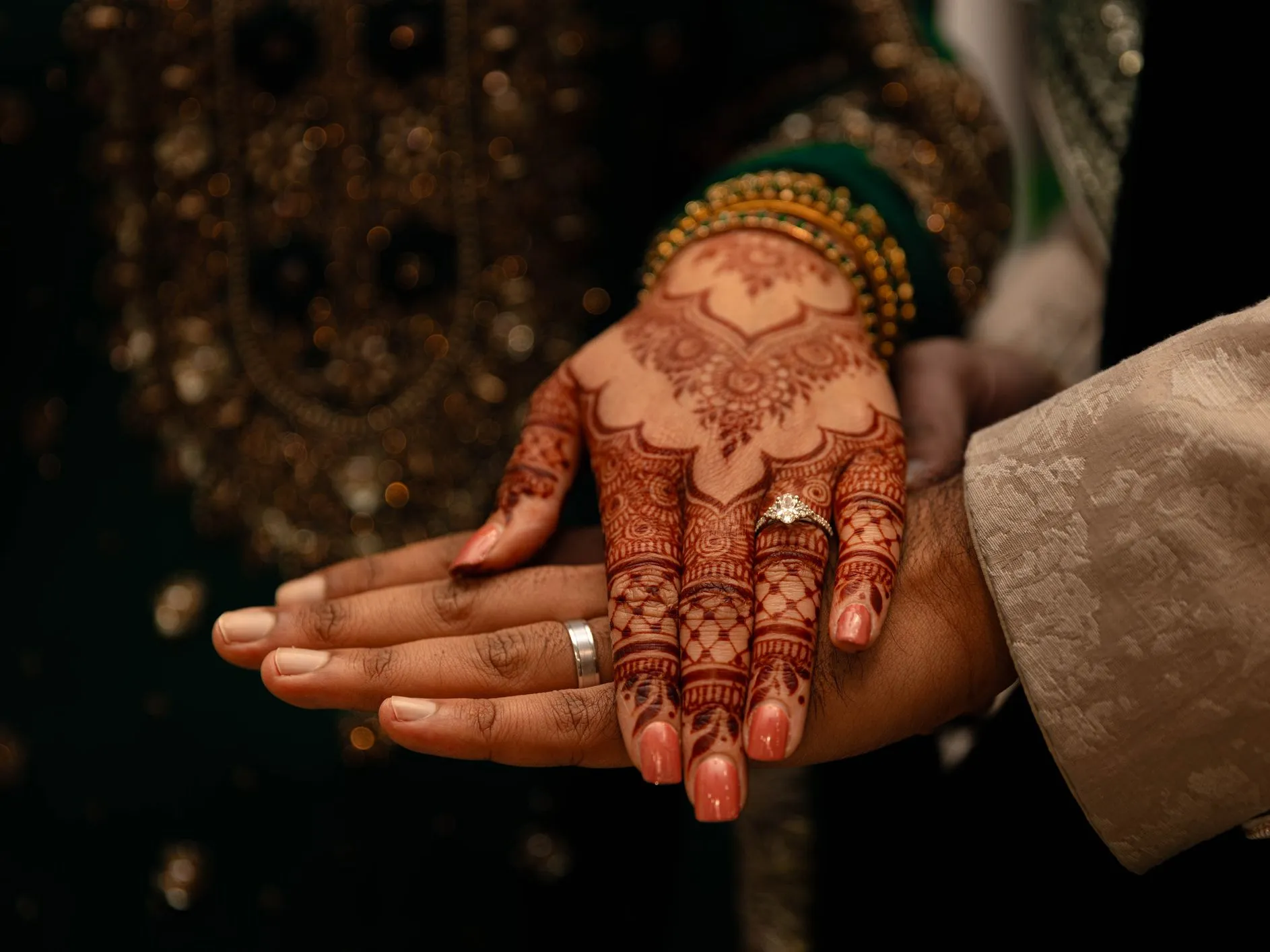 Close-up of a bride’s mehndi-covered hand with an engagement ring resting on a partner’s hand during a traditional wedding ceremony.