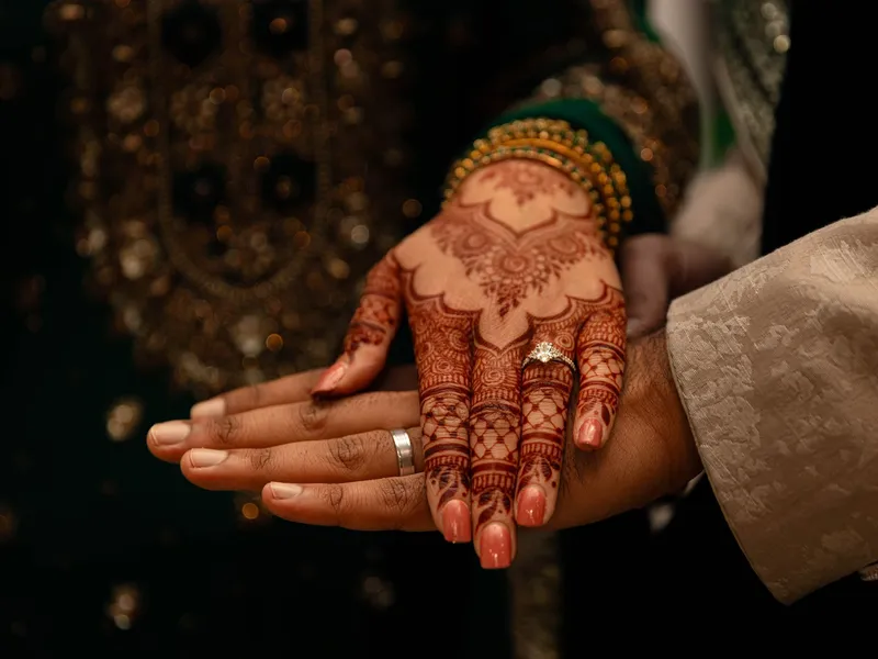 Close-up of a bride’s mehndi-covered hand with an engagement ring resting on a partner’s hand during a traditional wedding ceremony.