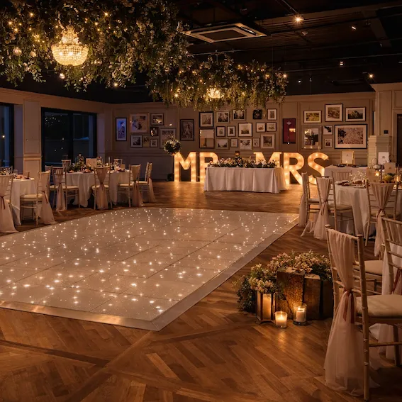 Elegant wedding reception venue with a sparkling dance floor, floral ceiling installations, chandeliers, and illuminated MR & MRS letters.