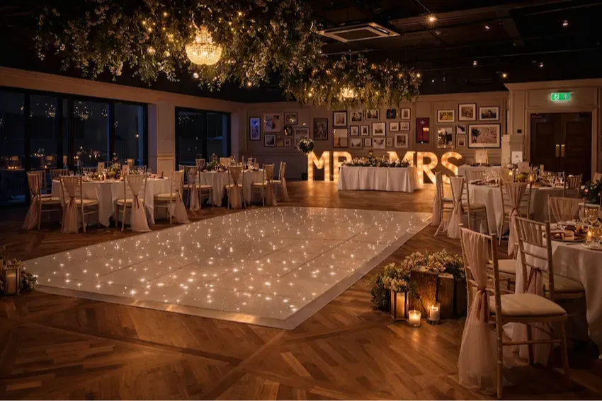 Elegant wedding reception venue with a sparkling dance floor, floral ceiling installations, chandeliers, and illuminated MR & MRS letters.