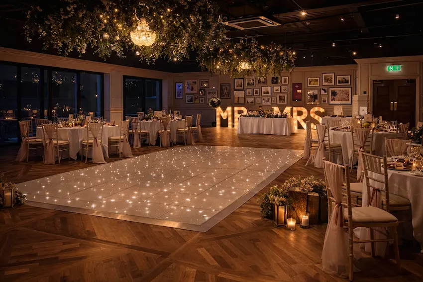 Elegant wedding reception venue with a sparkling dance floor, floral ceiling installations, chandeliers, and illuminated MR & MRS letters.