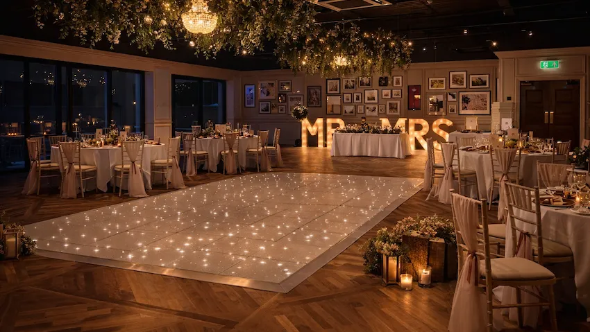 Elegant wedding reception venue with a sparkling dance floor, floral ceiling installations, chandeliers, and illuminated MR & MRS letters.