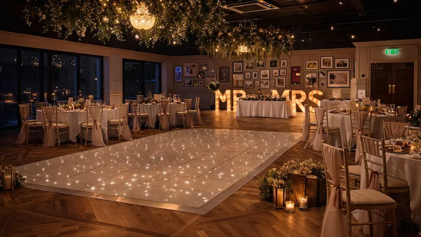 Elegant wedding reception venue with a sparkling dance floor, floral ceiling installations, chandeliers, and illuminated MR & MRS letters.
