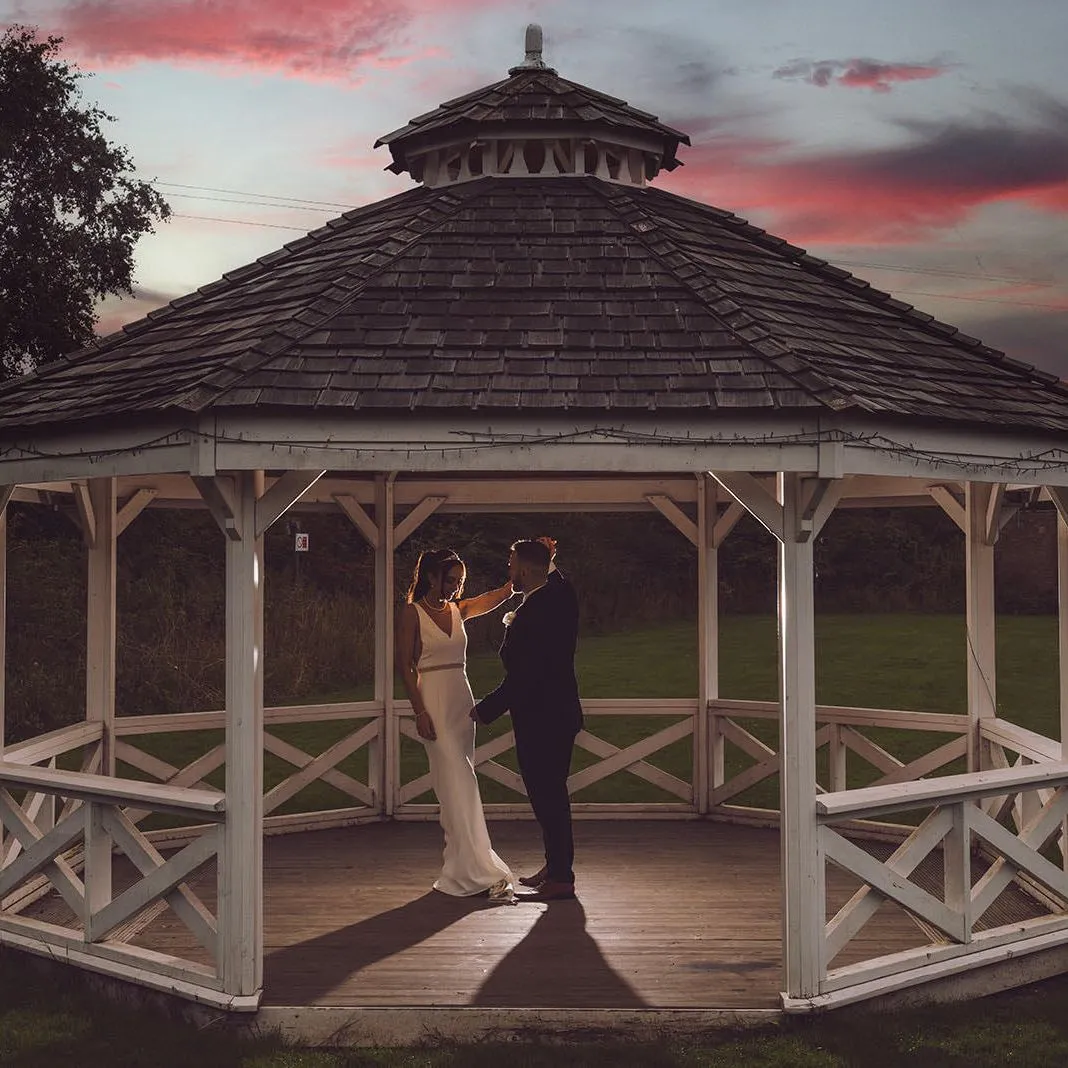 Bride and groom standing in a white wooden gazebo at sunset