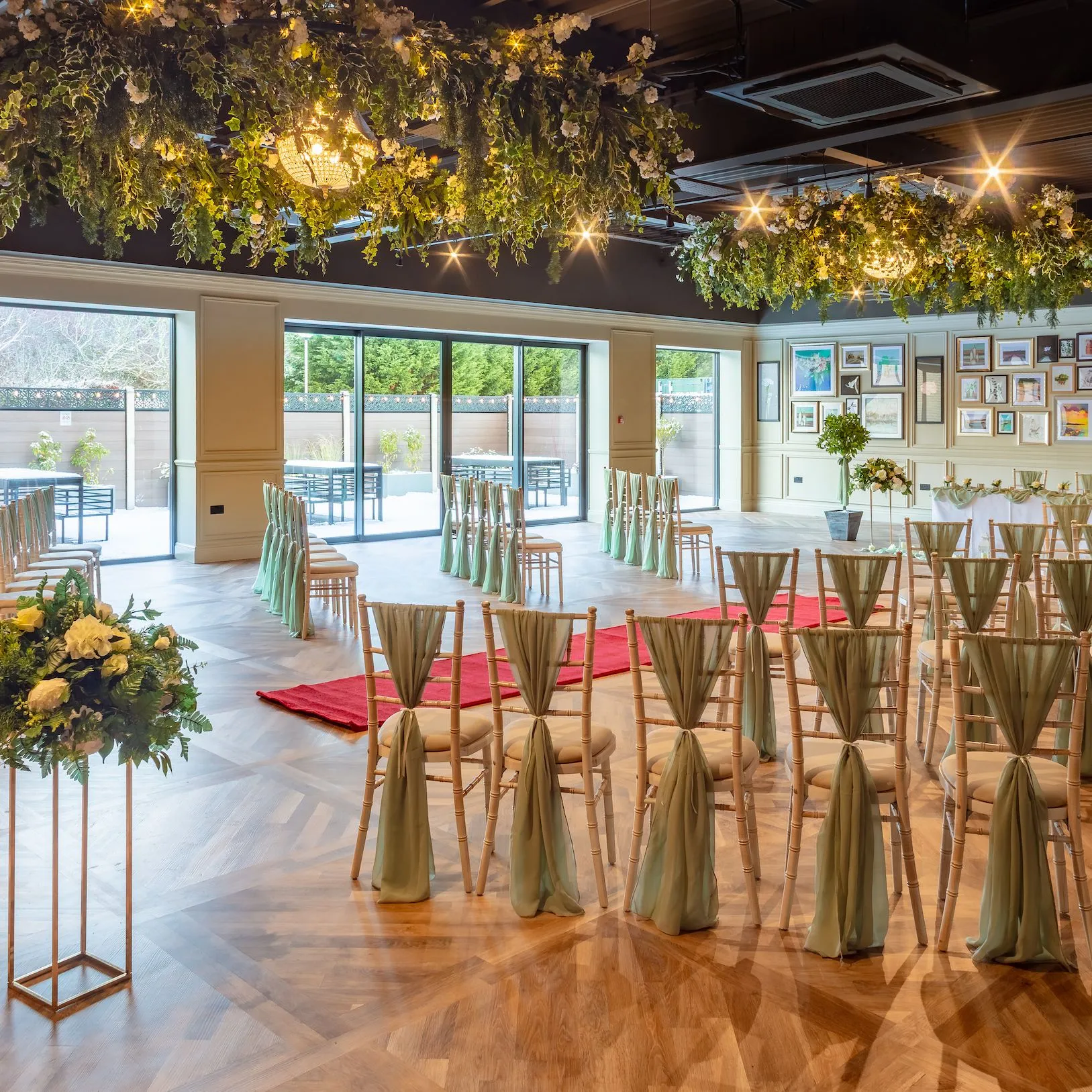 Elegant indoor wedding ceremony setup with floral ceiling installations, rose arrangements and rows of chairs in a stylish hotel venue
