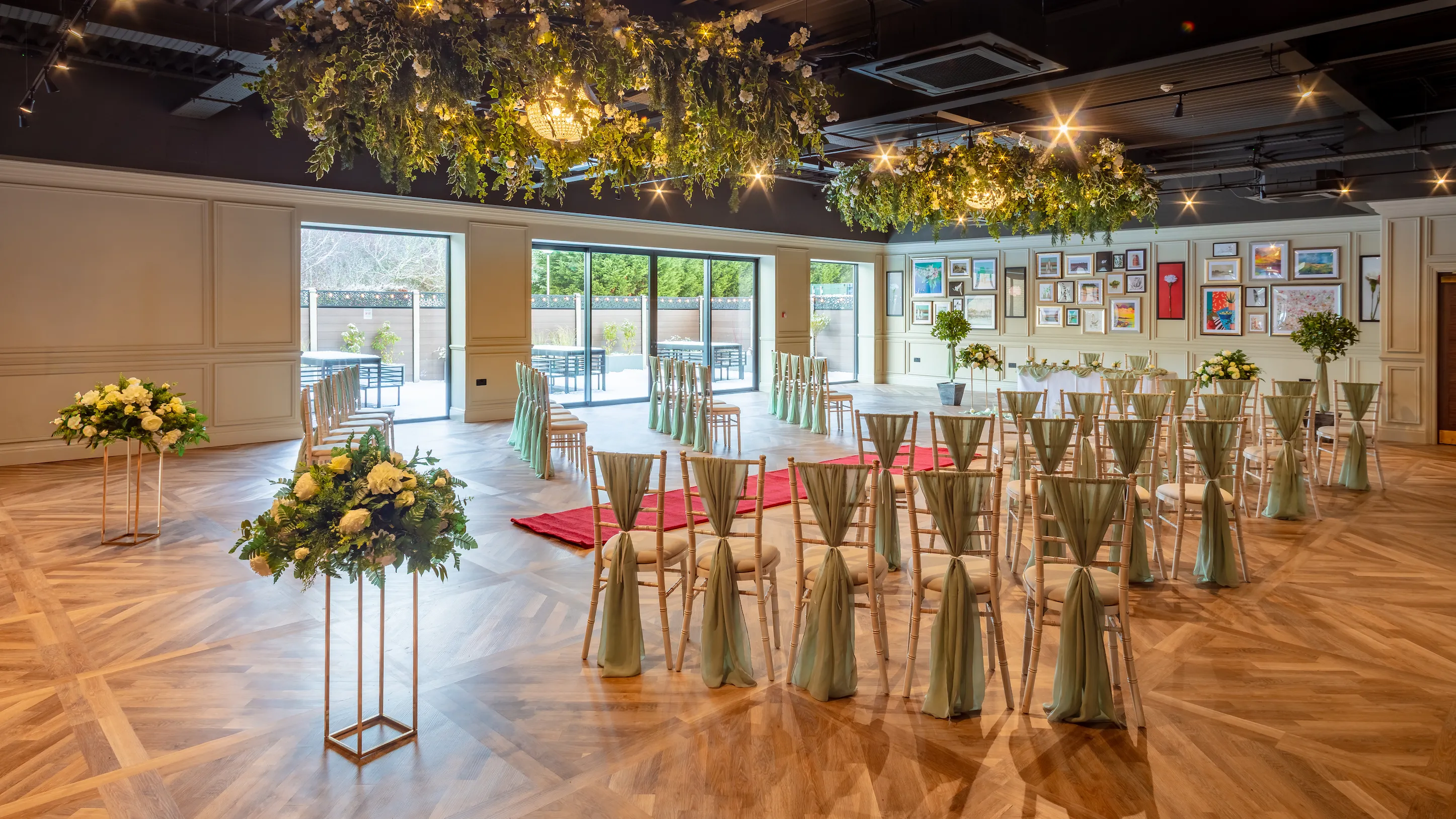 Elegant indoor wedding ceremony setup with floral ceiling installations, rose arrangements and rows of chairs in a stylish hotel venue