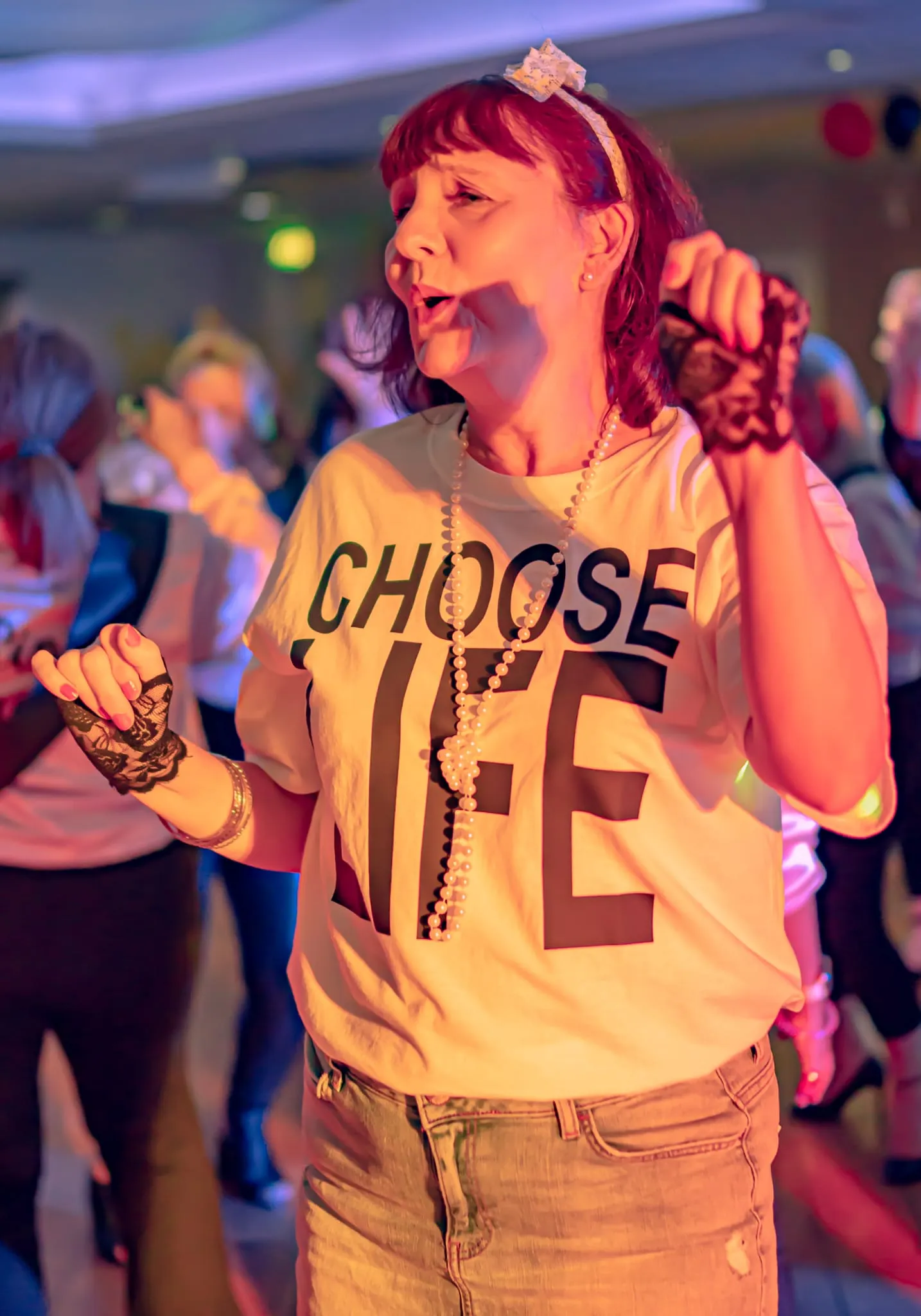 Woman dancing at a lively party wearing a white 'Choose Life' T-shirt, pearl necklace and lace gloves