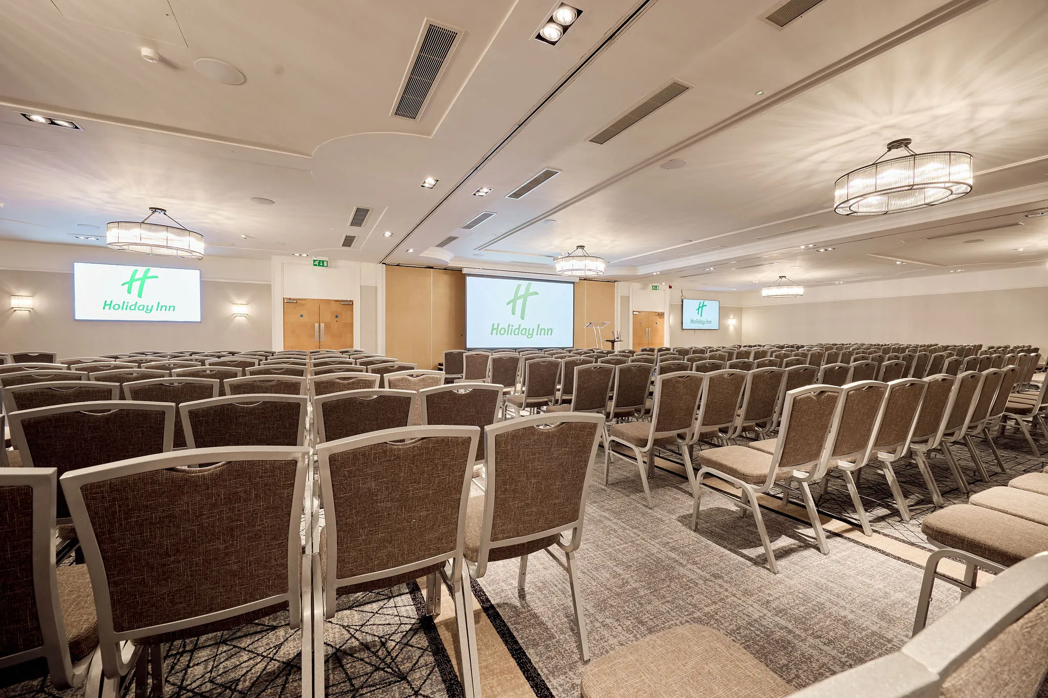 Conference room set up theatre-style with rows of chairs, projection screens and lectern at Holiday Inn