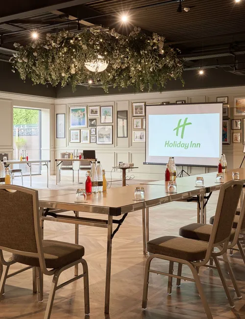 Meeting room at Holiday Inn with U-shaped conference layout, projector screen and floral ceiling décor