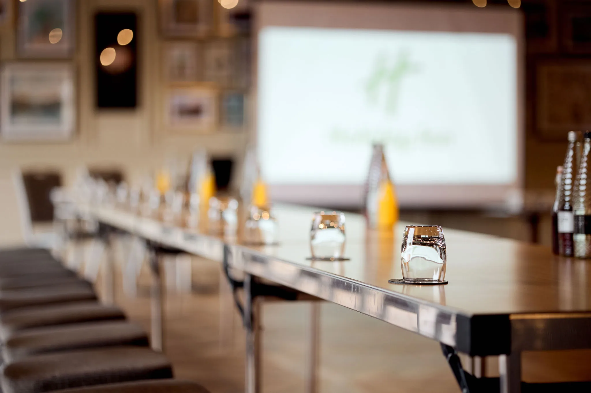 Conference room set up with long tables, water glasses and a projection screen in the background