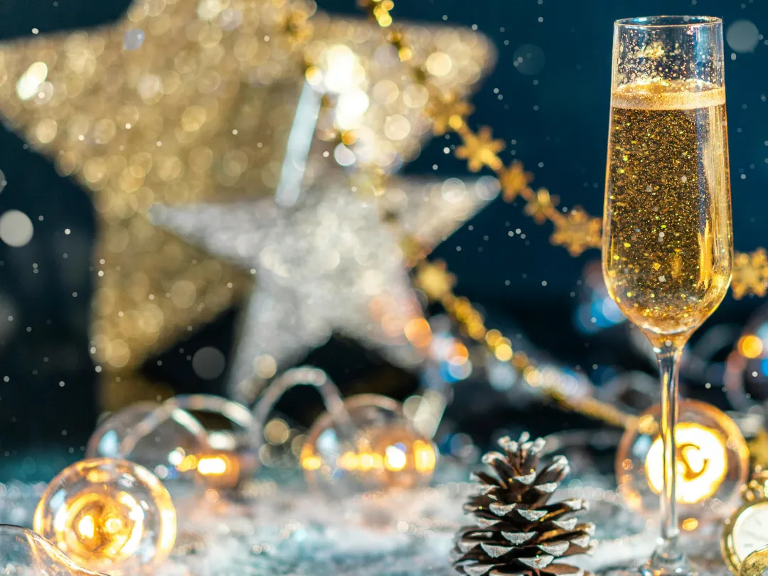 Glass of sparkling champagne on a festive New Year's Eve table with glowing fairy lights, star decorations and snow-like glitter.