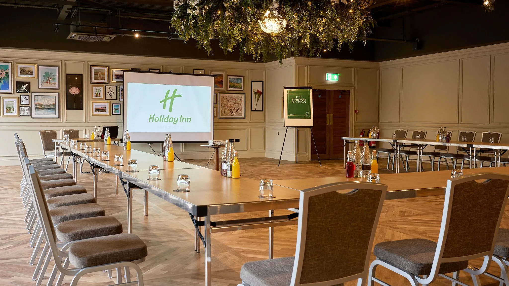 Meeting room set up in a U-shape with tables, chairs, bottled drinks and a presentation screen at Holiday Inn.